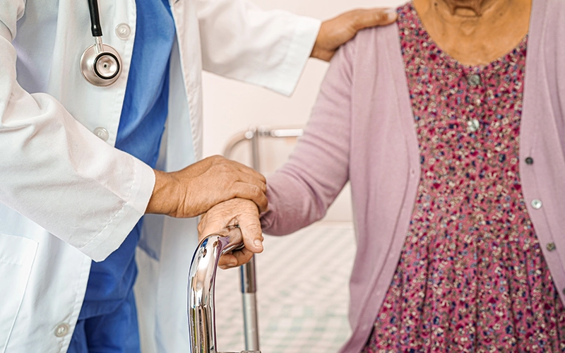 רופא עוזר למטופלת לעמוד בעזרת הליכון ותומך בה